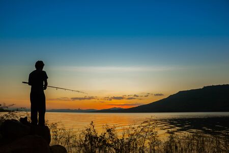 Silhouette a man standing fishing at lake with mountain background at sunset time location at north east of Thailandの写真素材