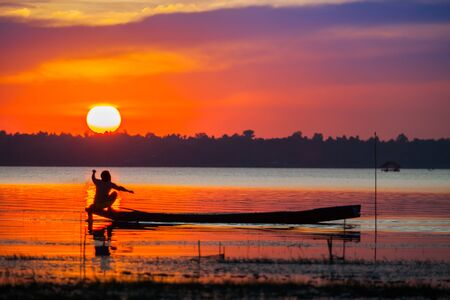 A silhouette of long boat with background beautiful of sunset colorful sky reflect on water in dam location at north east of Thailandの写真素材