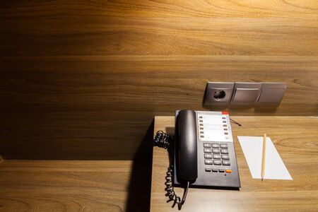 telephone on wooden table under light and note