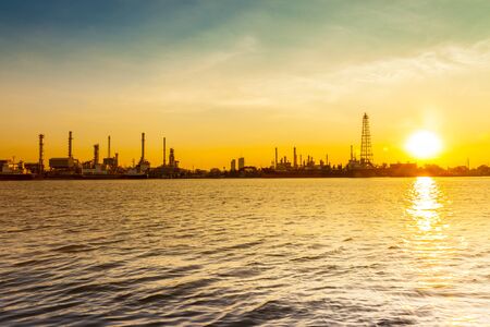 Oil refinery industry reflection on water at early morning under colorful sky of sunrise