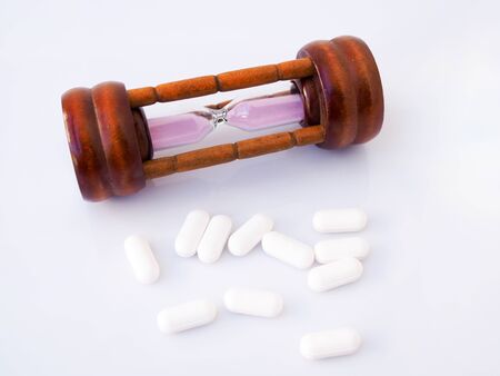Hourglass and painkiller, medicine tablets, time and health care concept. Isolated on white...