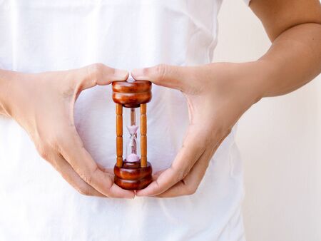 Young asian woman with hourglass in hand at belly, concept time of menstruation cramps and stomach...
