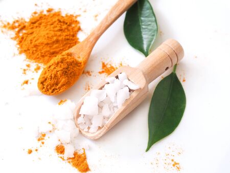 Top view of sea salt in scoop and turmeric powder in wooden spoon and green leaves isolated on white background.の写真素材