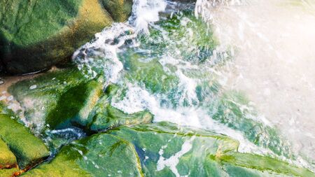 blurred waves of coastal water sea on rocks with green moss.の写真素材