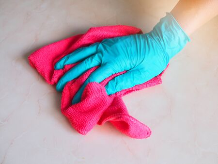 Cleaning in house with hand wearing rubber gloves and wiping dust with red cloth.