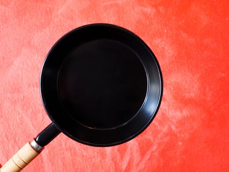 Top view of black frying pan on red cement wall background.の写真素材