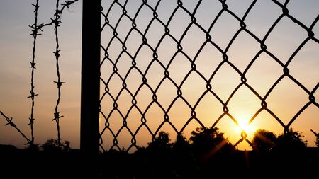 silhouette of mesh fence and barbed wire with dark sky at sunset.の写真素材