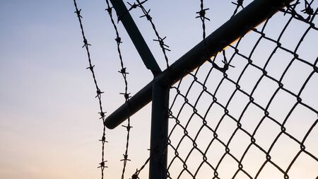 silhouette on metal mesh fence and barbed wire mesh at sunset.の写真素材