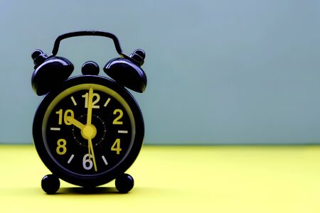 Black clock on blue yellow background with copy space.