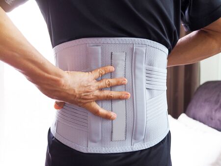 old man with back pain wearing back support belt or medical belt.