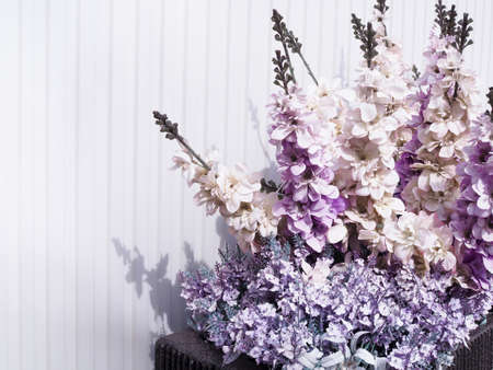 Beautiful vintage background scene with purple flowers in vase on white wall backdrop.