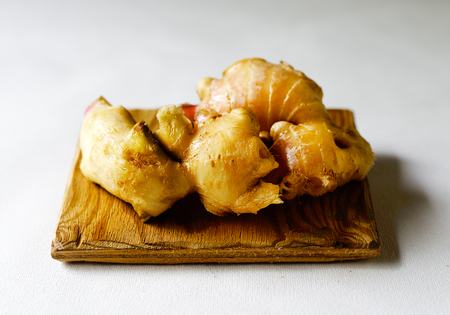 Fresh ginger on a wooden board against a white background.