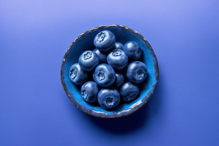 Blueberries in a blue bowl on a blue background, top viewの素材