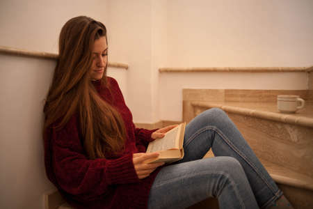 pretty young woman reading a book and drinking coffee happily. Woman with long brown hair reading a...