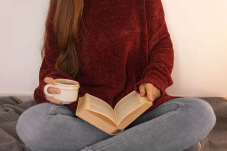 pretty young woman reading a book and drinking coffee happily. Woman with long brown hair reading a book. Woman sitting on some stairs.の写真素材
