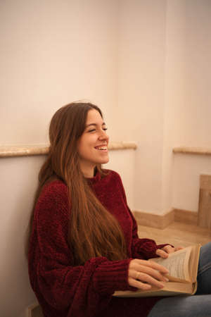 pretty young woman reading a book and drinking coffee happily. Woman with long brown hair reading a book. Woman sitting on some stairs.の写真素材