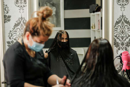 Woman with face mask getting a fresh style at a hair salon. Woman getting a hair wash. Hairdressing concept. Hairdresser cutting and styling a woman in her shopの写真素材
