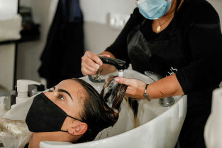 Woman with face mask getting a fresh style at a hair salon. Woman getting a hair wash. Hairdressing concept. Hairdresser cutting and styling a woman in her shopの写真素材