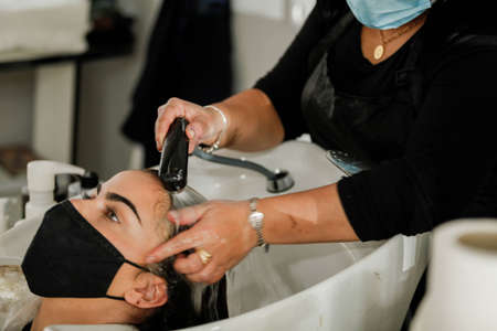 Woman with face mask getting a fresh style at a hair salon. Woman getting a hair wash. Hairdressing concept. Hairdresser cutting and styling a woman in her shopの写真素材