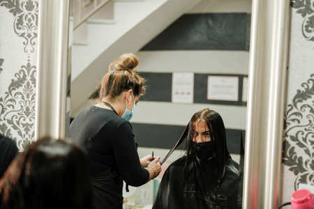 Woman with face mask getting a fresh style at a hair salon. Woman getting a hair wash. Hairdressing concept. Hairdresser cutting and styling a woman in her shopの写真素材