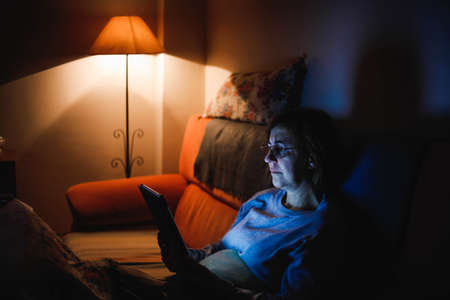 adult woman using a touch tablet in the living room. Adult woman using a touch device. Woman reading a book. Woman making video call with familyの写真素材