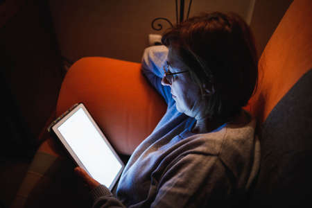 adult woman using a touch tablet in the living room. Adult woman using a touch device. Woman reading...