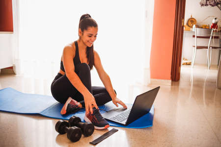 Woman exercising at home with laptop. Fit woman doing yoga plank and watching online tutorials on...