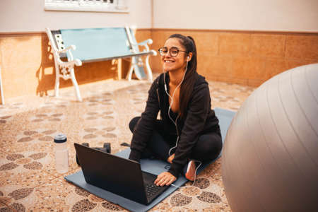 Woman exercising at home with laptop. Fit woman doing yoga plank and watching online tutorials on laptopの写真素材