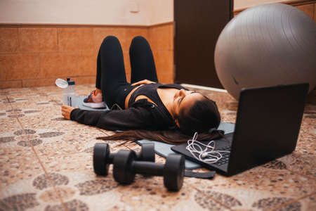 Woman exercising at home with laptop. Fit woman doing yoga plank and watching online tutorials on...