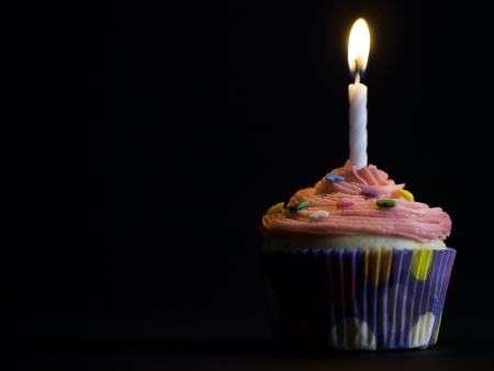 pink cupcake with candle on it and black background. Perfect dessert for a birthday. Shallow depth of field.の写真素材