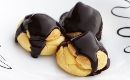 three sweets profiteroles dessert on a white plate.