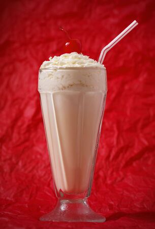 vanilla milkshake with whipped cream and cherry on the top. Focus on the cherry. Red background.の写真素材