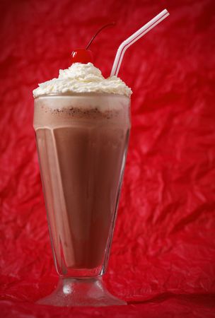 chocolate milkshake with whipped cream and cherry on the top. Focus on the cherry. Red background.の写真素材
