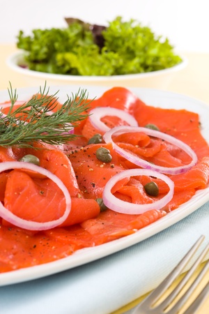 Appetizer smoked salmon with caper, spice and salad in the background. Very shallow depth of field. の写真素材