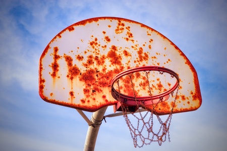 Old and rusty basketball basket with a cloudy blue sky in the background.の写真素材
