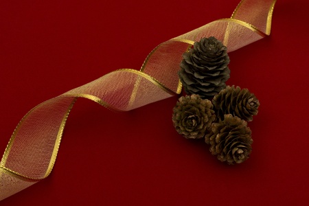 Christmas decoration background/wallpaper with golden ribbon and pine cones on red fabric.