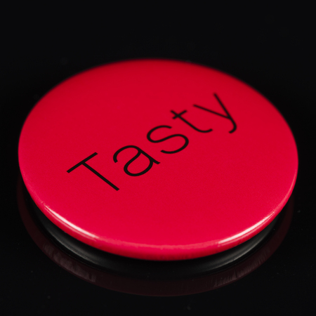 Magnetic red button with the word 'tasty' written on it on a black background with reflections.の写真素材