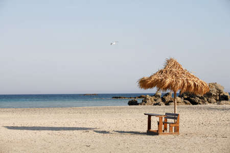 A desk and thatched umbrella sit inconguously on Elafonissos beach, Crete. An ideal place for doing holiday homework or catching up on your backlog at work, scrutinised by a passing seagull.の写真素材