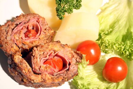 Slices of beef roulade (rolled beef meatloaf) served with potato, lettuce and cherry tomato. The roulade is wrapped around ham and tomatoes.の写真素材