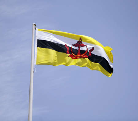 The national flag of the Sultanate of Brunei against a blue sky with thin cloud.の写真素材