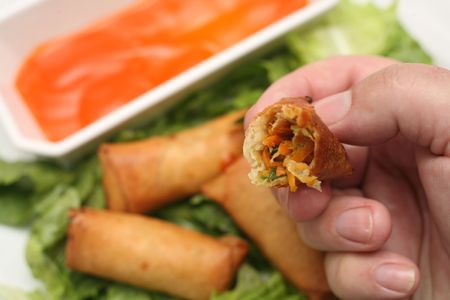 Eating a vegetable spring roll, with other spring rolls in the background on a bed of lettuce,...