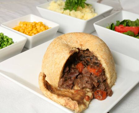 A steak and kidney pudding, with a steamed suet crust, on a buffet with salad, peas, sweetcorn and...