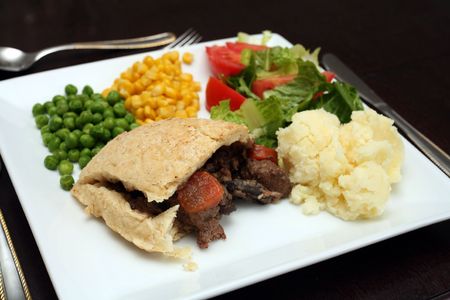 A steak, kidney, mushroom and carrot pudding, in a suet pastry crust, served with lettuce, potatoes,...