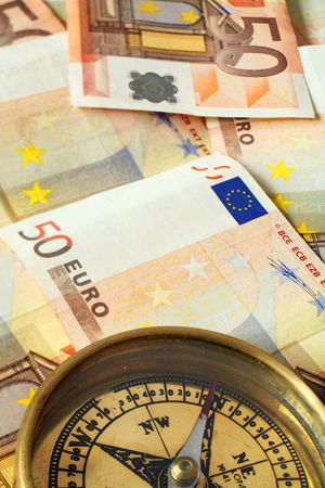 A compass, its needle pointing north, on a pile of 50 euro notes, symbolising investment being on track.の写真素材