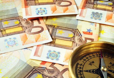 A compass, its needle pointing North, on a background of 50 euro notes, symbolising finances going in the right direction.の写真素材