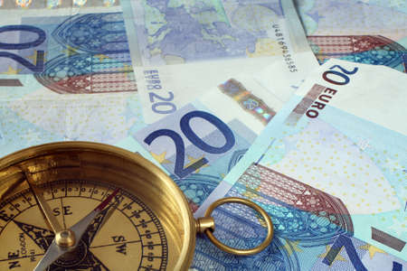 A compass, its needle pointing south, on a pile of 20 Euro notes.の写真素材