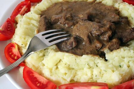 Beef stroganoff served on a bed of creamed parsley potato, ringed by wedges of small organic tomatoes.の写真素材