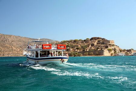 A pleasure boat takes day=trippers to Spinalonga island fortress, Crete - a Venetian castle that became  Greece's 20th Century leper colonyの写真素材