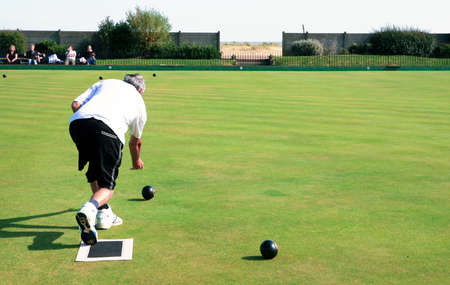 A bowler playing on the village green. Bowls is a traditional British game. The faces of the spectators are unrecognisable.の写真素材