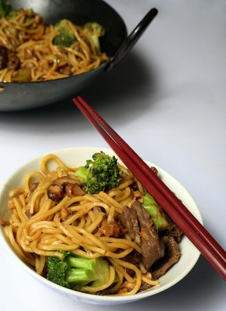 Beef chow mein and chopsticks, with the wok in the background.の写真素材